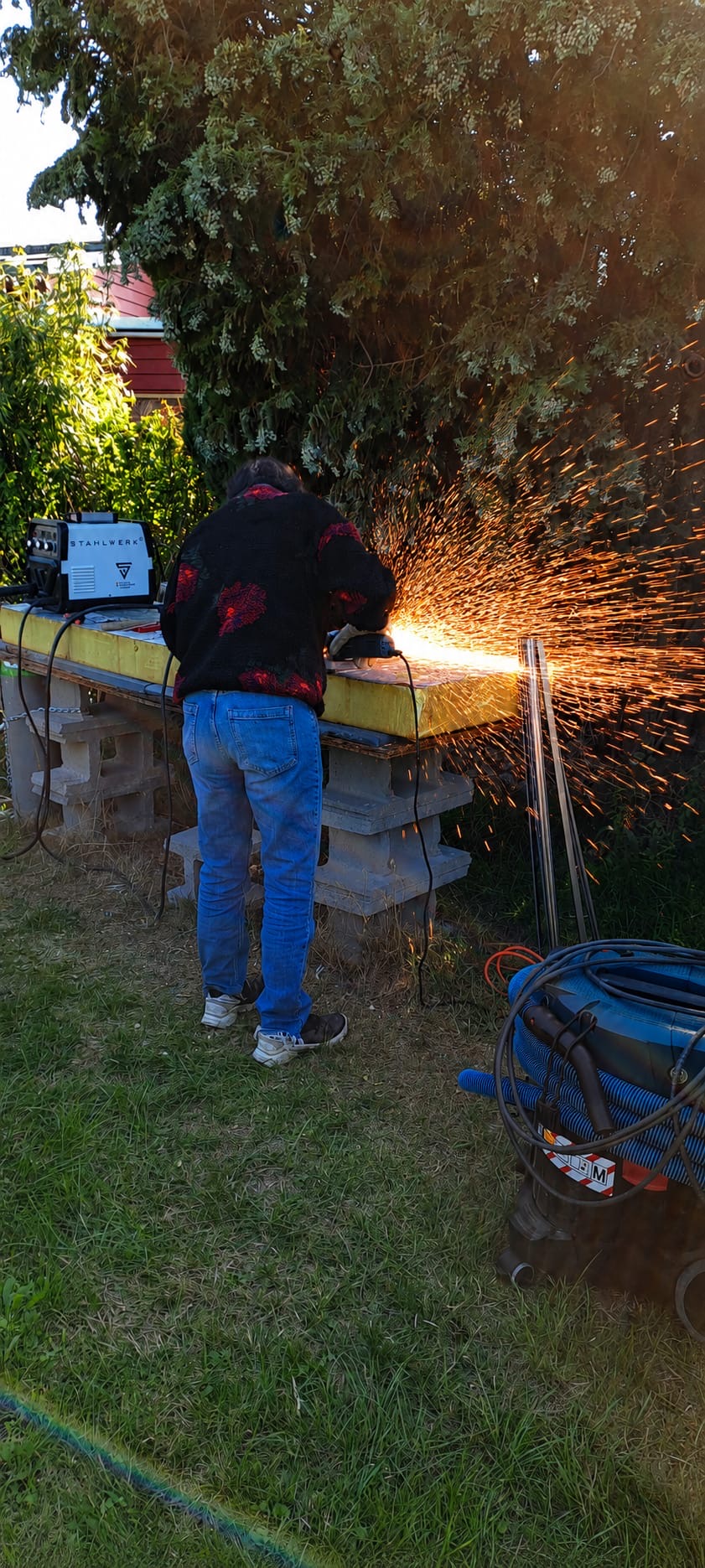 Metallbearbeitung: Eine Person bearbeitet ein Metallteil mit einem Winkelschleifer an seiner Werkbank im Freien